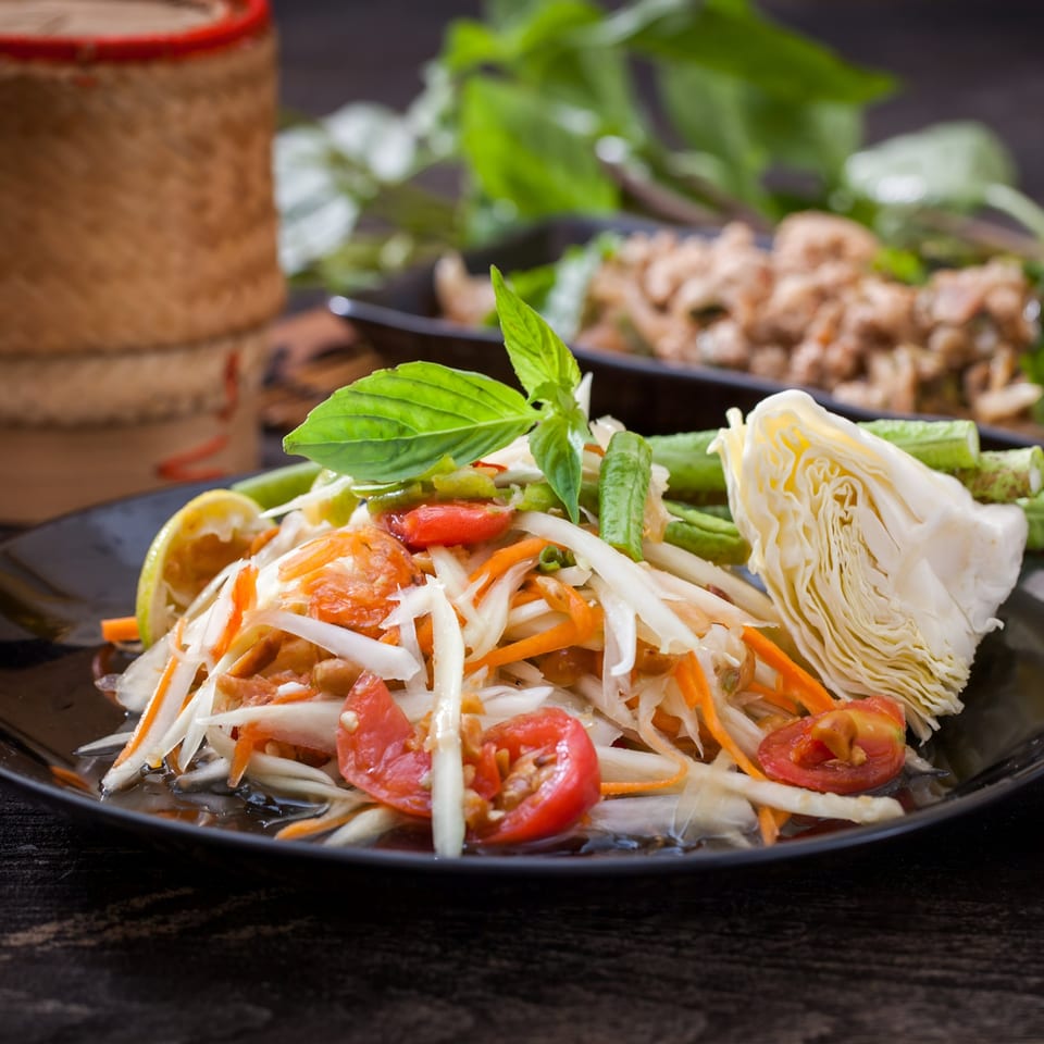 Som Tum (papaya salad) with tomatoes, cabbage, and green beans on a black plate.