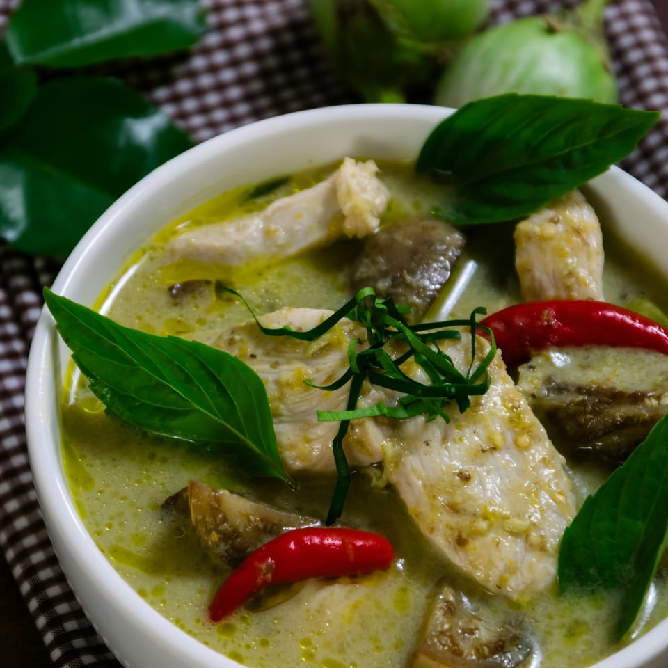 Close-up of Kati Thai Eatery's green curry with chicken, red chilies, and basil in a white bowl.