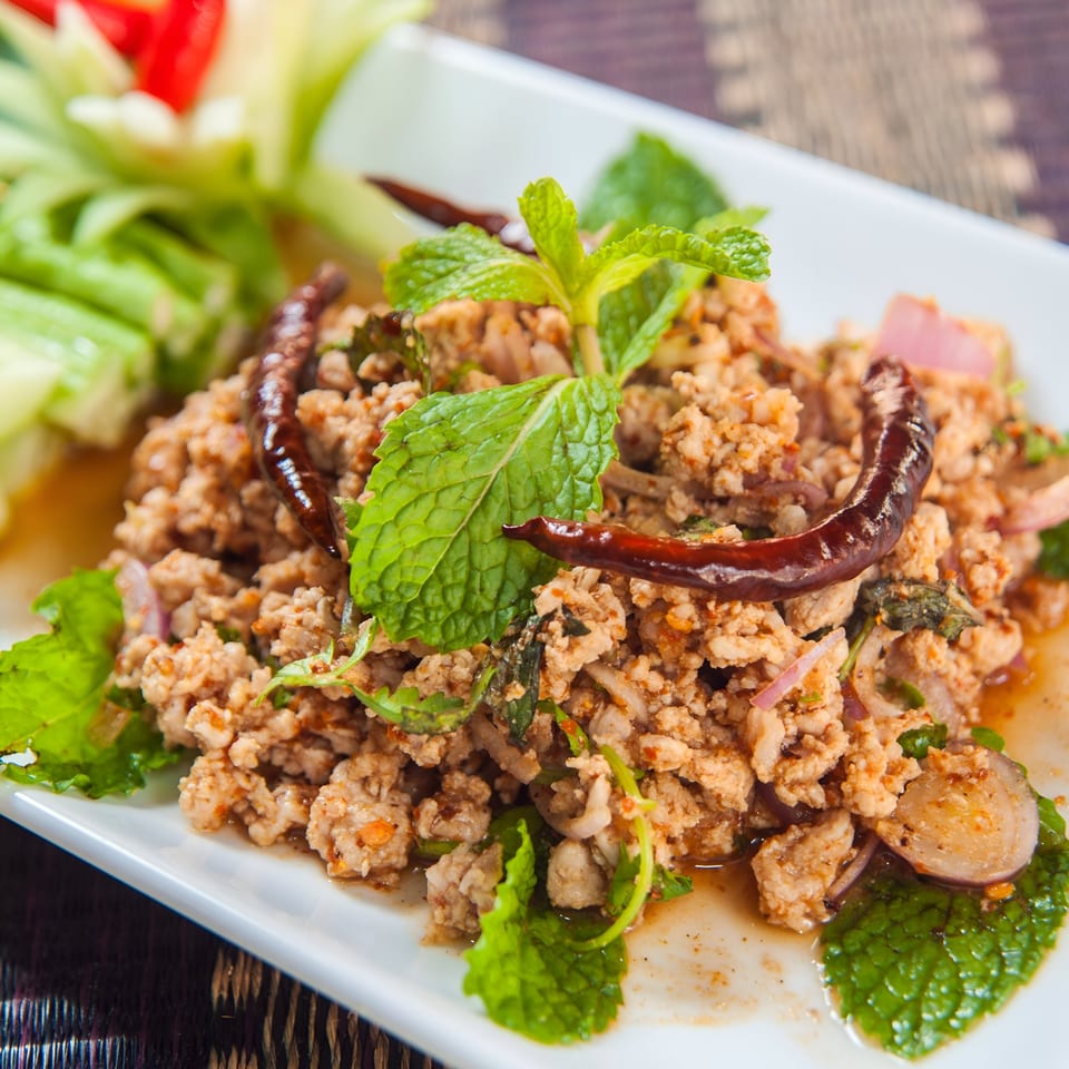 Close-up of a Thai Larb dish with minced meat, mint, red onions, and dried chilies.
