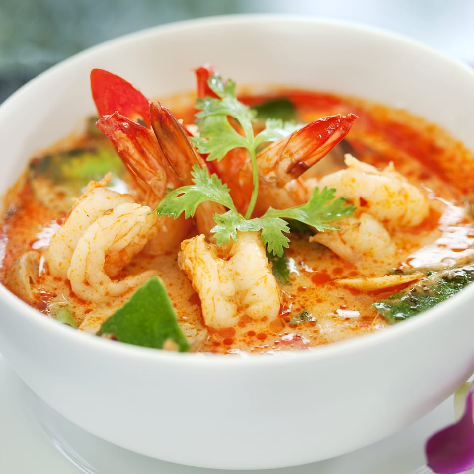 Close-up of Tom Yum Goong, a spicy Thai shrimp soup, garnished with cilantro and chili.
